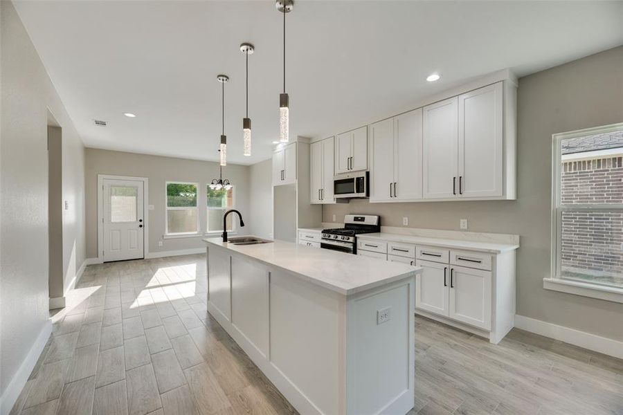 Kitchen featuring white cabinets, decorative light fixtures, appliances with stainless steel finishes, and sink