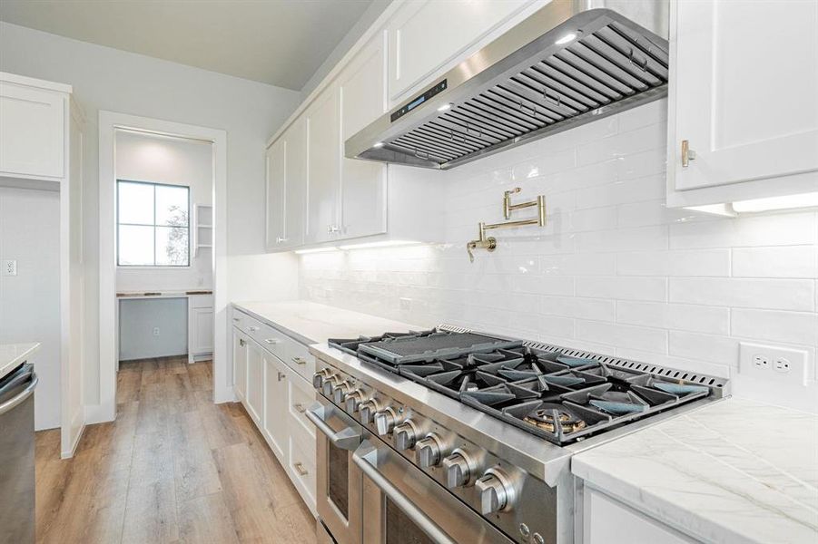 Kitchen with white cabinetry, light hardwood / wood-style floors, wall chimney range hood, and appliances with stainless steel finishes