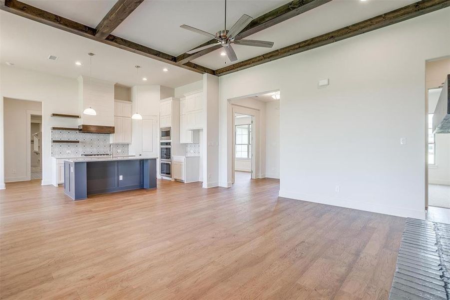 Unfurnished living room with beamed ceiling, ceiling fan, and light hardwood / wood-style flooring