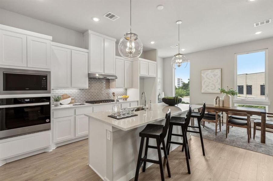 Kitchen with a kitchen island with sink, backsplash, appliances with stainless steel finishes, and light wood-type flooring