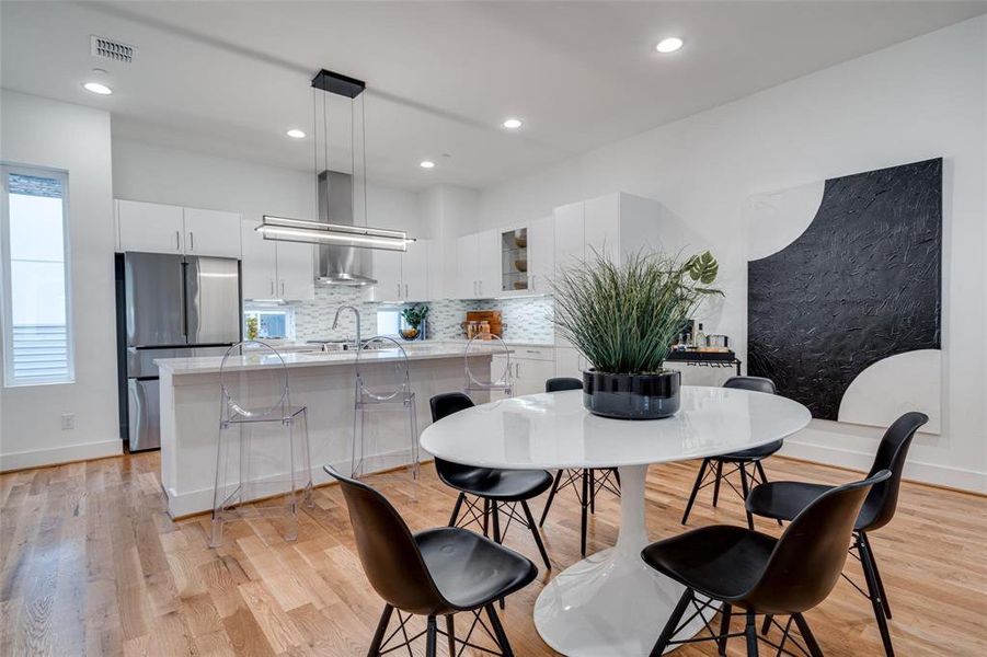 Kitchen with white cabinets, stainless steel fridge, wall chimney exhaust hood, a breakfast bar area, and light hardwood / wood-style floors