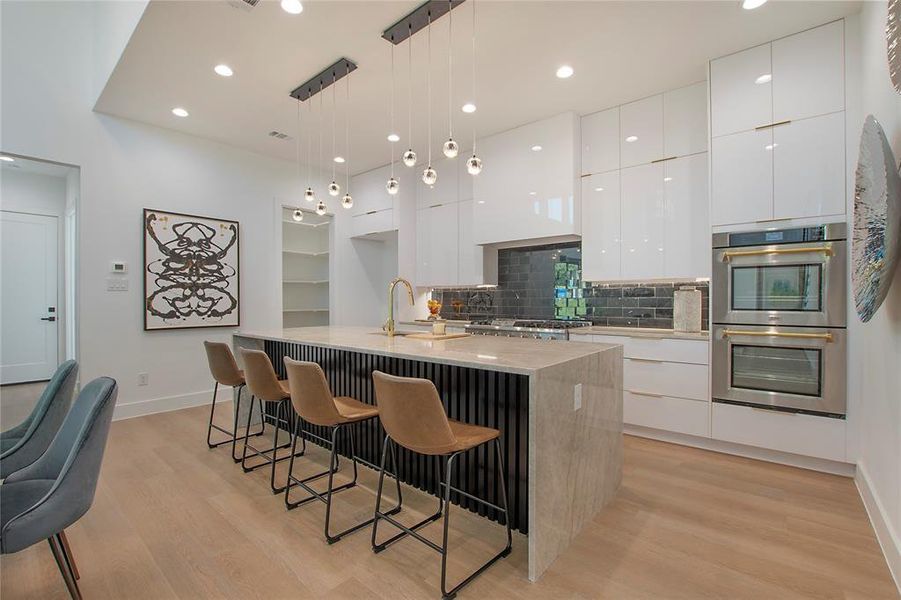 Kitchen with an island with sink, white cabinets, hanging light fixtures, and light wood-type flooring