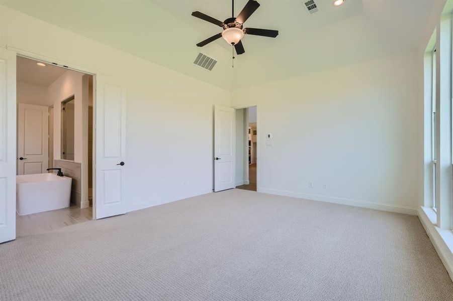 Unfurnished bedroom featuring ensuite bathroom, lofted ceiling, light colored carpet, and ceiling fan