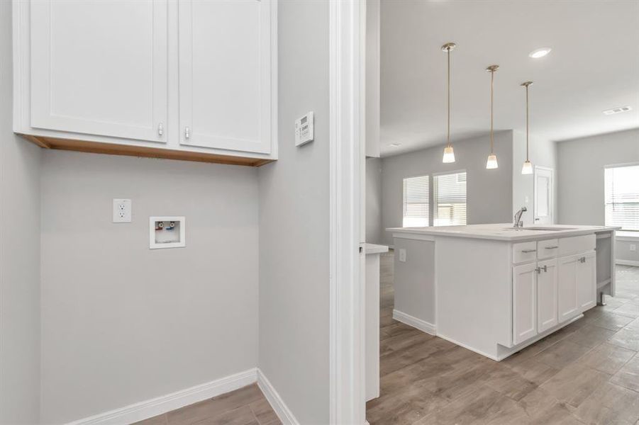 This convenient laundry area, located just off the kitchen, offers both functionality and easy access. Featuring upper cabinetry for additional storage, this space is designed to make household chores a breeze. The open view into the kitchen and living areas ensures that you can keep an eye on everything while multitasking, making it perfect for a busy household. **This image is from another Saratoga Home with similar floor plan and finishes, not the June floorplan.**