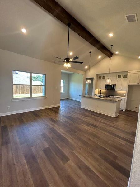 Unfurnished living room with vaulted ceiling with beams, ceiling fan, dark wood-type flooring, and sink