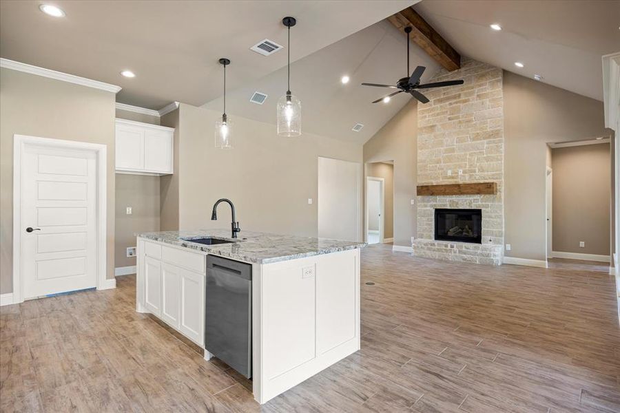 Kitchen with light stone counters, an island with sink, white cabinetry, light wood-type flooring, and sink