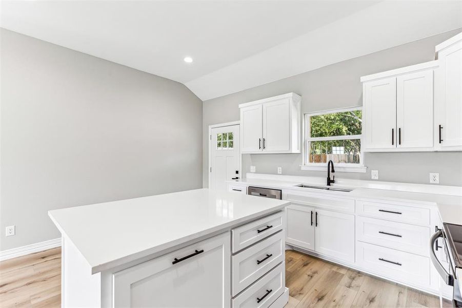 Kitchen with white cabinetry, light hardwood / wood-style flooring, a kitchen island, sink, and lofted ceiling