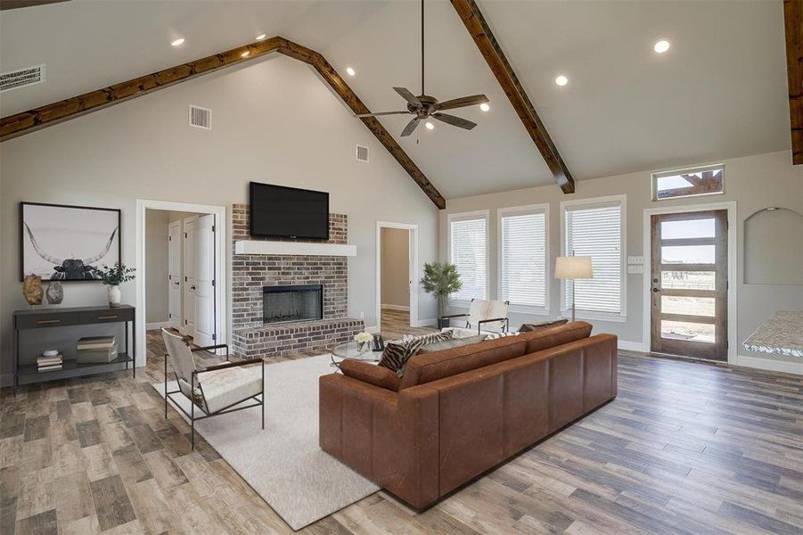 Living room featuring a fireplace, ceiling fan, beam ceiling, high vaulted ceiling, and light hardwood / wood-style flooring