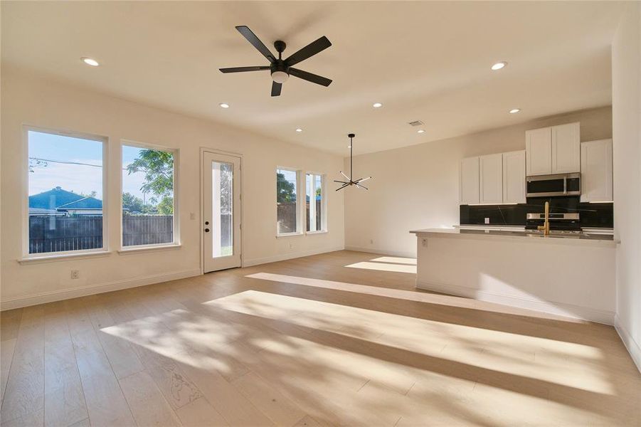 Unfurnished living room with ceiling fan with notable chandelier and light hardwood / wood-style flooring