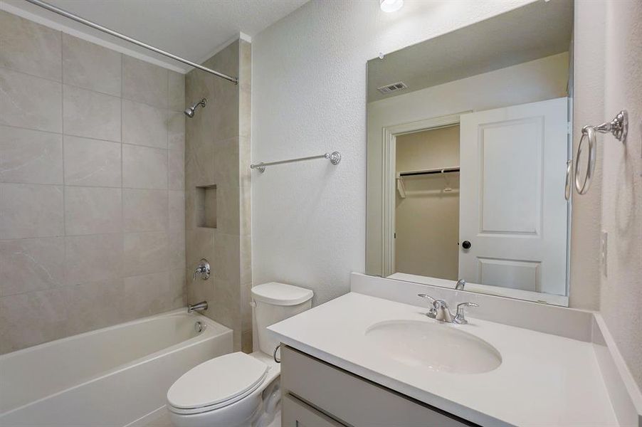 Full bathroom with vanity with extensive cabinet space, toilet, and tiled shower / bath combo