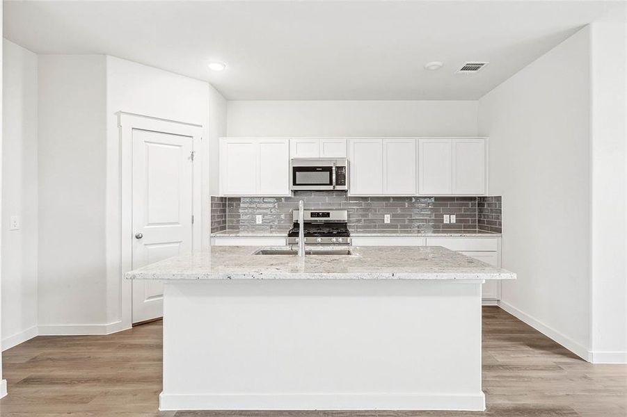 Kitchen with white cabinetry, light hardwood / wood-style floors, appliances with stainless steel finishes, and a center island with sink