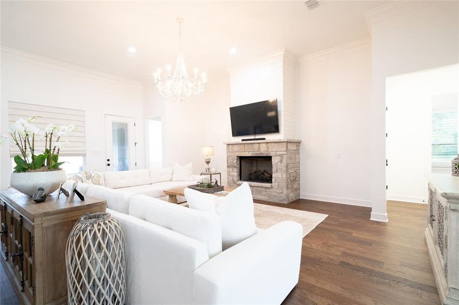 Living room featuring ornamental molding, a stone fireplace, an inviting chandelier, and dark hardwood / wood-style flooring