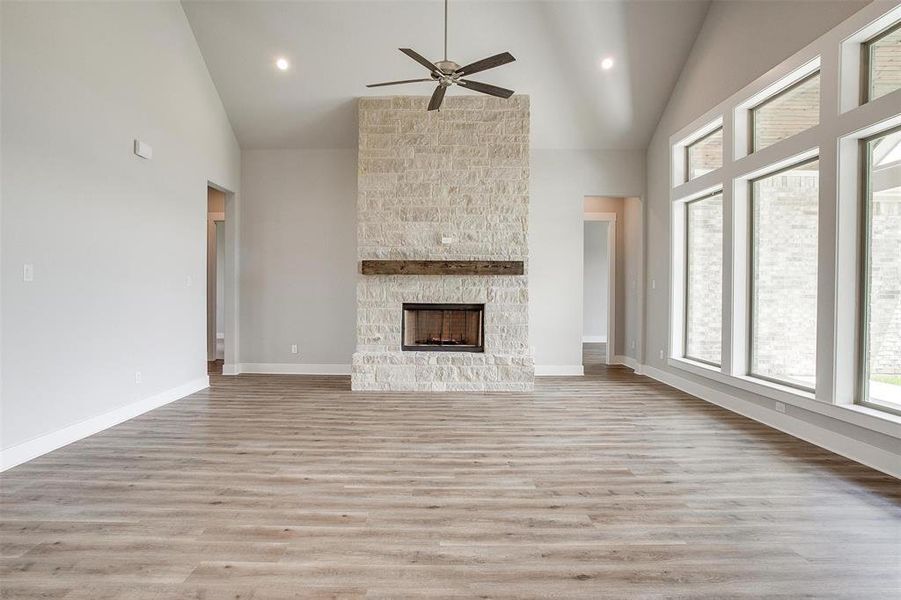 Unfurnished living room featuring a stone fireplace, high vaulted ceiling, light wood-type flooring, and ceiling fan