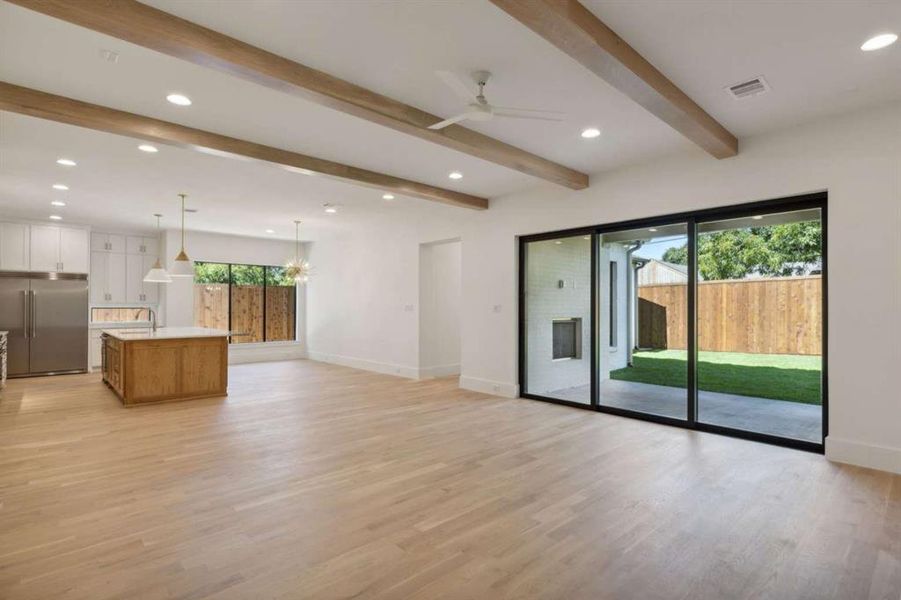 Unfurnished living room featuring ceiling fan with notable chandelier, beamed ceiling, sink, and light hardwood / wood-style flooring