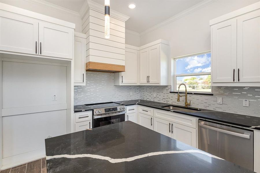 Kitchen with sink, backsplash, white cabinetry, appliances with stainless steel finishes, and crown molding