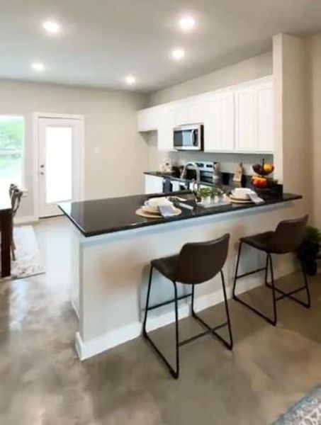 Kitchen with stainless steel appliances, kitchen peninsula, a kitchen breakfast bar, and white cabinetry