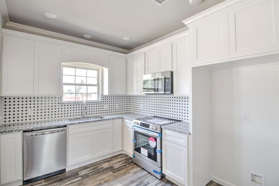 Kitchen with white cabinetry, appliances with stainless steel finishes, wood-type flooring, sink, and tasteful backsplash