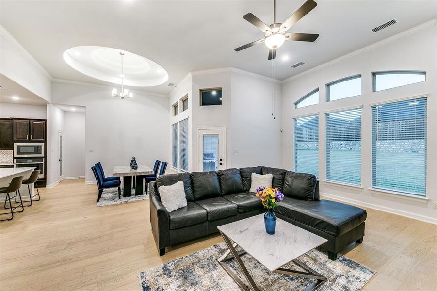 Living room with light hardwood / wood-style floors, crown molding, ceiling fan with notable chandelier, and a towering ceiling