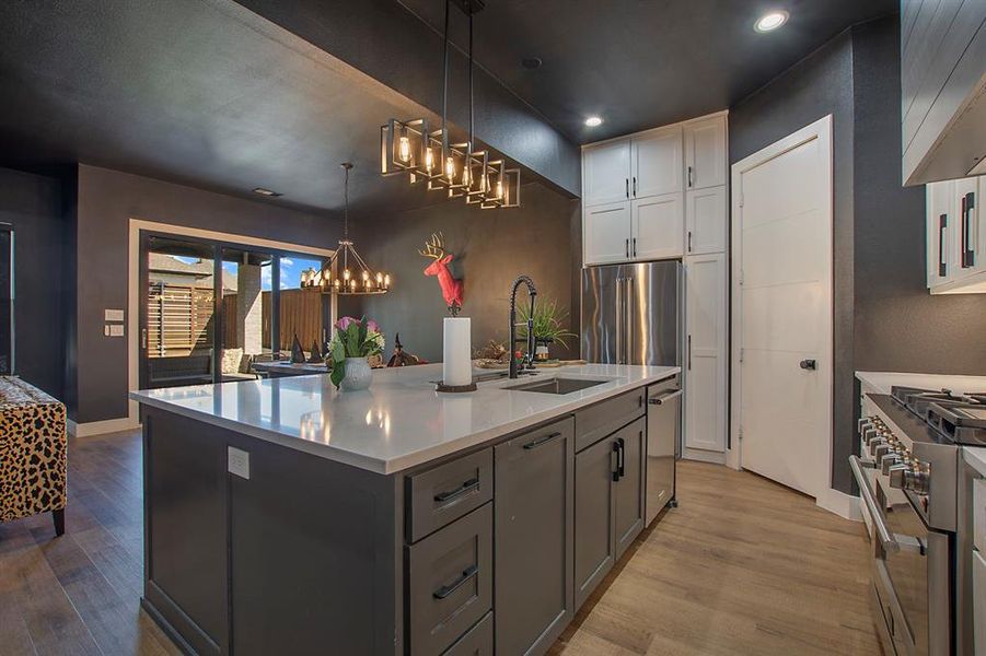 Kitchen featuring high quality appliances, an island with sink, hanging light fixtures, sink, and white cabinetry