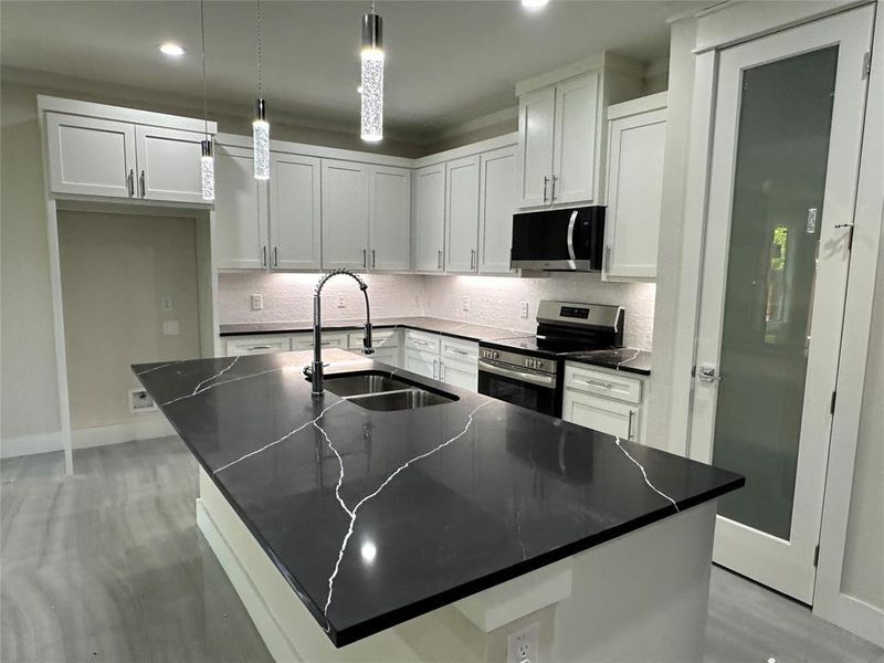 Kitchen with an island with sink, pendant lighting, sink, white cabinets, and appliances with stainless steel finishes