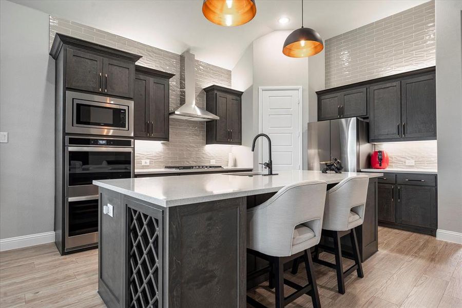 Kitchen with wall chimney range hood, appliances with stainless steel finishes, tasteful backsplash, and light hardwood / wood-style floors