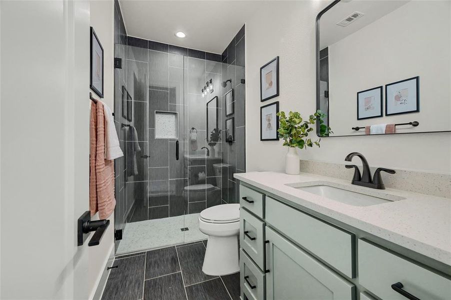 Bathroom featuring vanity, quartz counters, framed mirror, tile floors, frameless glass shower