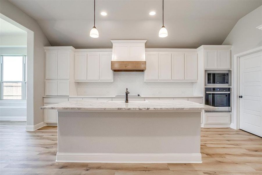 Kitchen with lofted ceiling, white cabinetry, light wood-type flooring, stainless steel appliances, and a center island with sink