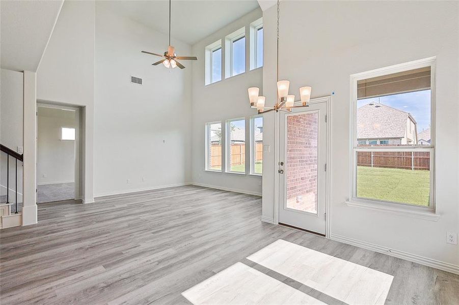 Unfurnished living room with high vaulted ceiling, ceiling fan with notable chandelier, and light hardwood / wood-style floors