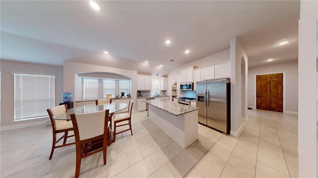 Kitchen featuring appliances with stainless steel finishes, white cabinets, light stone countertops, light tile patterned floors, and a kitchen island with sink