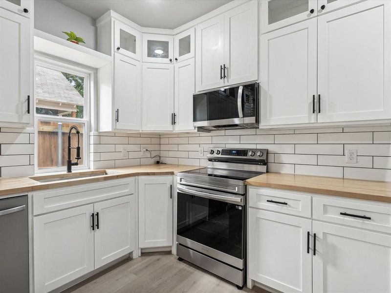 Kitchen with sink, appliances with stainless steel finishes, white cabinetry, and light hardwood / wood-style floors