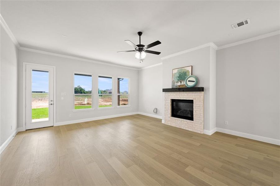 Unfurnished living room featuring a brick fireplace, light hardwood / wood-style flooring, ceiling fan, and a wealth of natural light