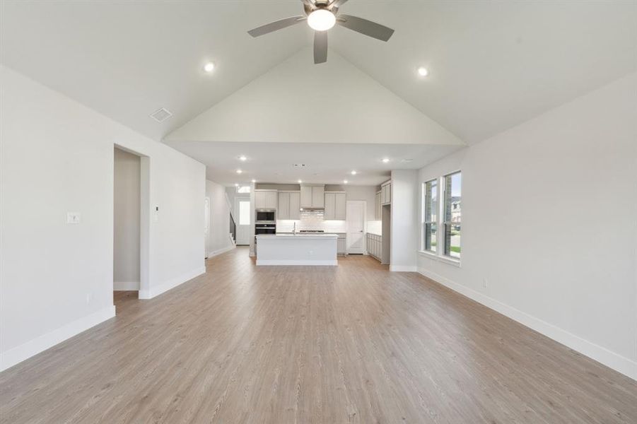 Unfurnished living room featuring light wood-type flooring, high vaulted ceiling, and ceiling fan