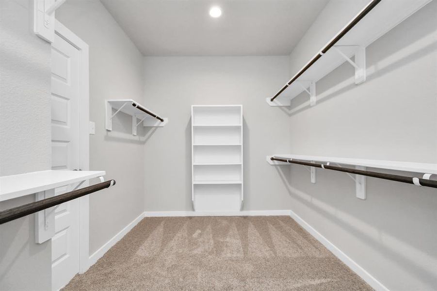 Expansive walk-in closet, adorned with high ceilings, luxurious carpet, and built in shelves. Sample photo of completed home with similar plan. As built color and selections may vary.