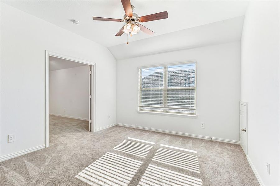 Carpeted spare room featuring vaulted ceiling and ceiling fan