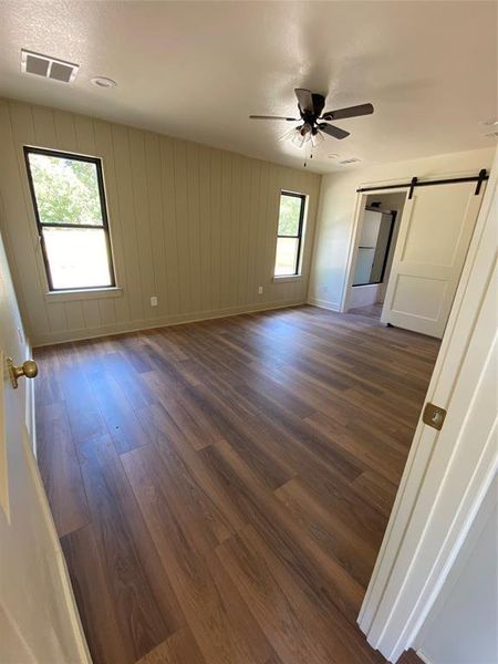 Master bedroom featuring dark wood-type flooring, a barn door, wood walls, a textured ceiling, and ceiling fan