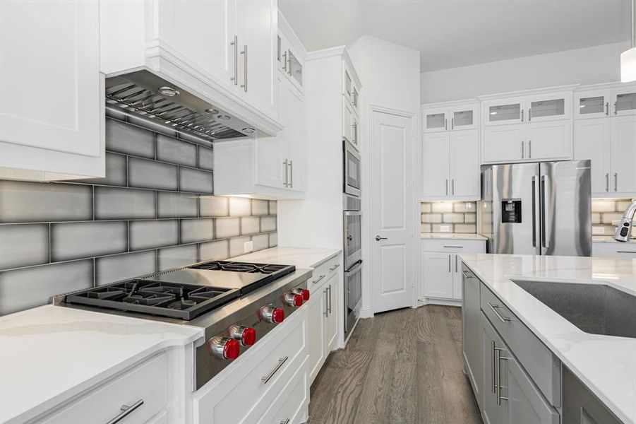 Kitchen with dark hardwood / wood-style floors, stainless steel appliances, tasteful backsplash, white cabinetry, and sink