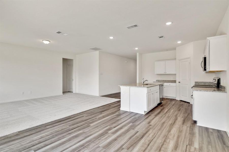 Kitchen with white cabinets, sink, a kitchen island with sink, light hardwood / wood-style flooring, and light stone countertops