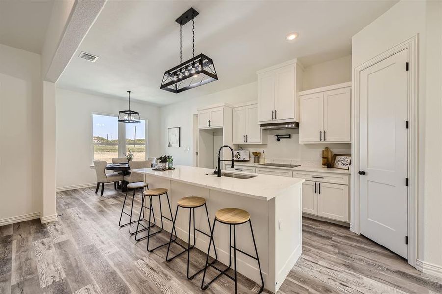 Kitchen featuring white cabinets, light hardwood / wood-style floors, and a center island with sink