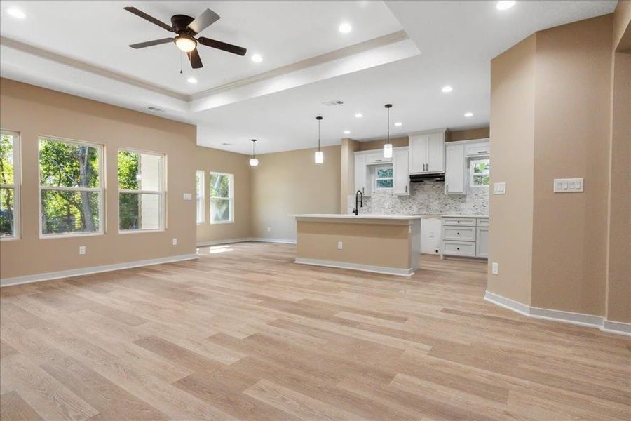 Kitchen featuring a center island with sink, white cabinets, tasteful backsplash, light wood-type flooring, and decorative light fixtures