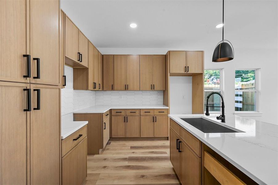 Kitchen with light stone countertops, light hardwood / wood-style floors, pendant lighting, backsplash, and sink