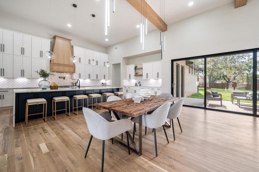 Dining space featuring light wood-type flooring, sink, beam ceiling, and a towering ceiling