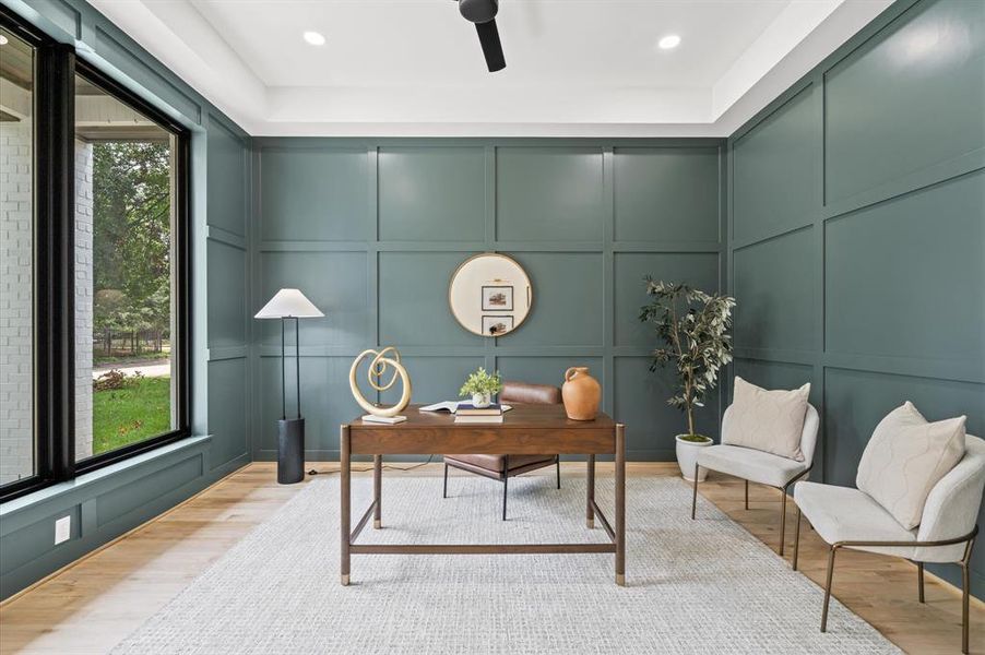 Elegant home office with custom paneled walls, and a view of the outdoors through large windows.