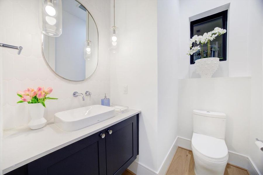 Powder Room with a Floating Cabinet, Slab Quartz Counter, White Vessel Sink, Wall-Mounted Faucet.  The backsplash wall is adorned with 3 x 8 Fishscale Matte Tile.  There is also a Framed Mirror and Two 11" Opal Capsule Pendants.