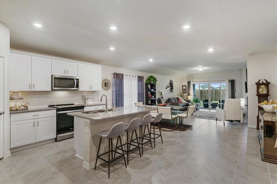 Kitchen featuring white cabinetry, appliances with stainless steel appliances, satin nickel finishes, and an island with breakfast bar.