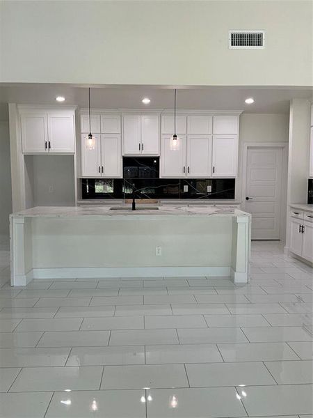 Kitchen featuring hanging light fixtures, light tile patterned flooring, white cabinetry, and backsplash