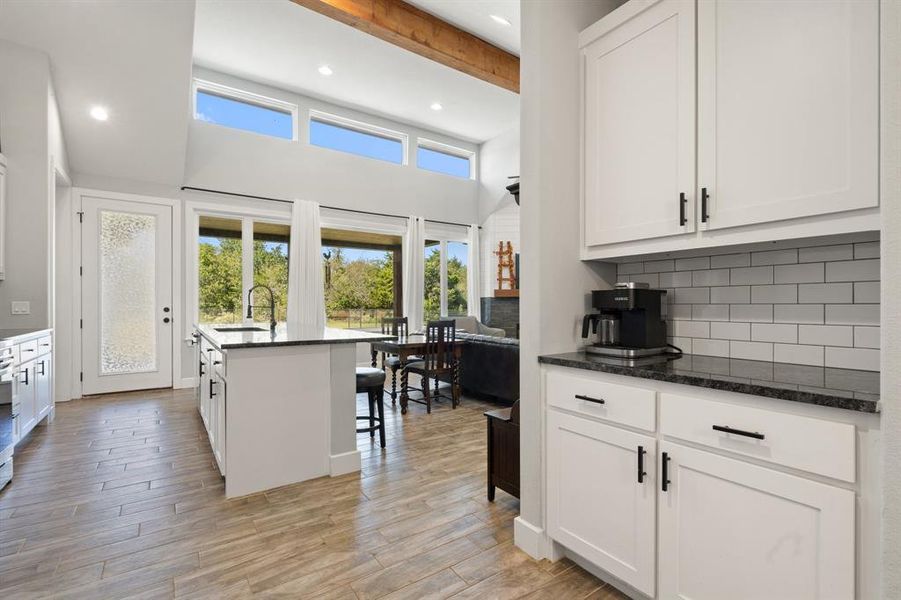 Kitchen featuring a kitchen island with sink, sink, beam ceiling, light hardwood / wood-style flooring, and dark stone countertops