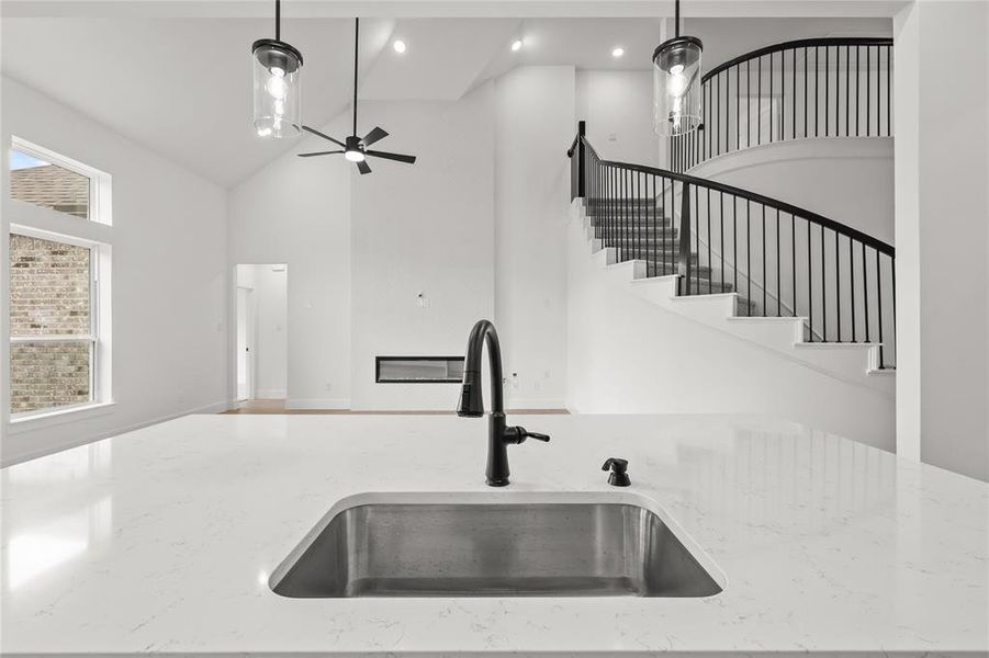 Kitchen featuring high vaulted ceiling, light stone countertops, sink, and decorative light fixtures