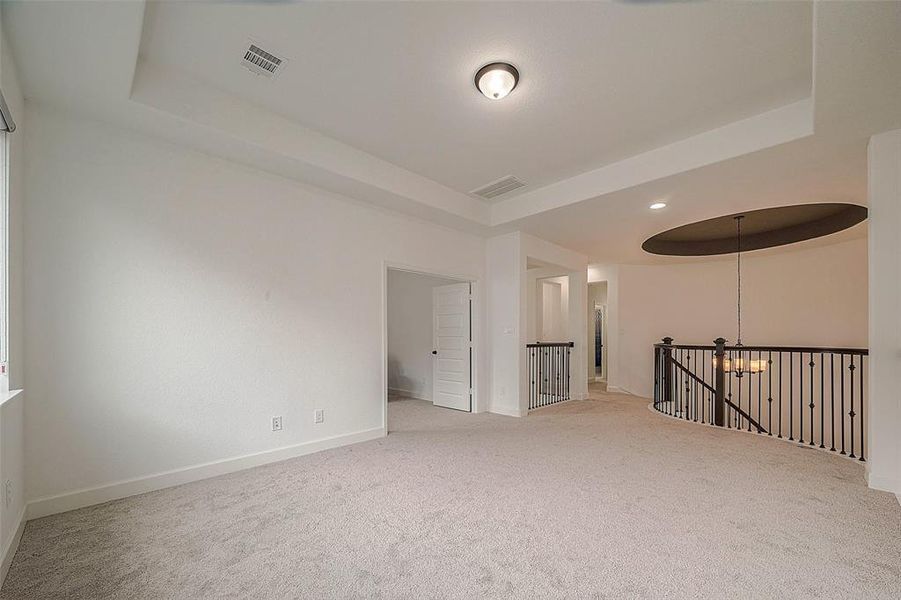 This spacious, well-lit upper-level room features plush carpeting, a vaulted ceiling, and a modern railing overlooking the lower level. Two doorways lead to other rooms, providing a flexible layout ideal for a variety of uses.