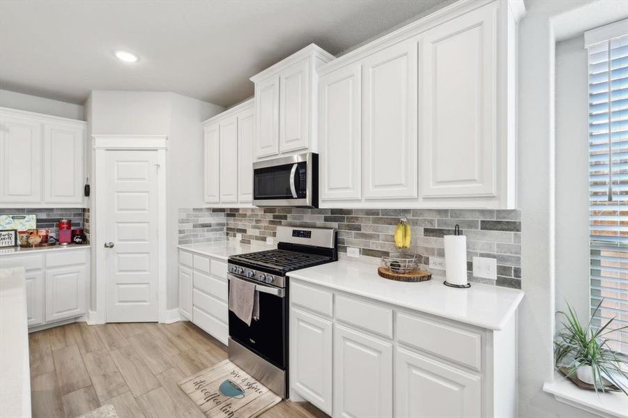 Kitchen with light wood-type flooring, decorative backsplash, white cabinetry, and stainless steel appliances