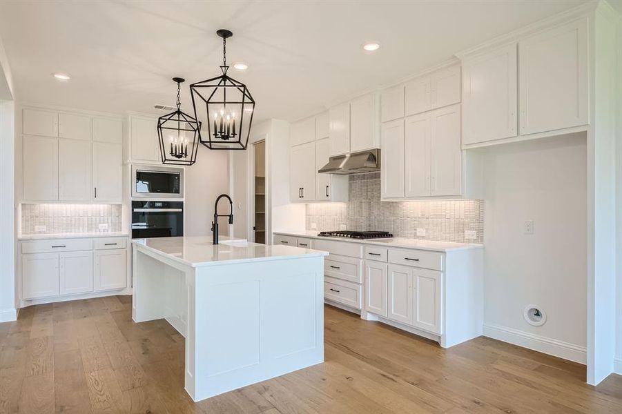 Kitchen with wall chimney exhaust hood, backsplash, black oven, and built in microwave